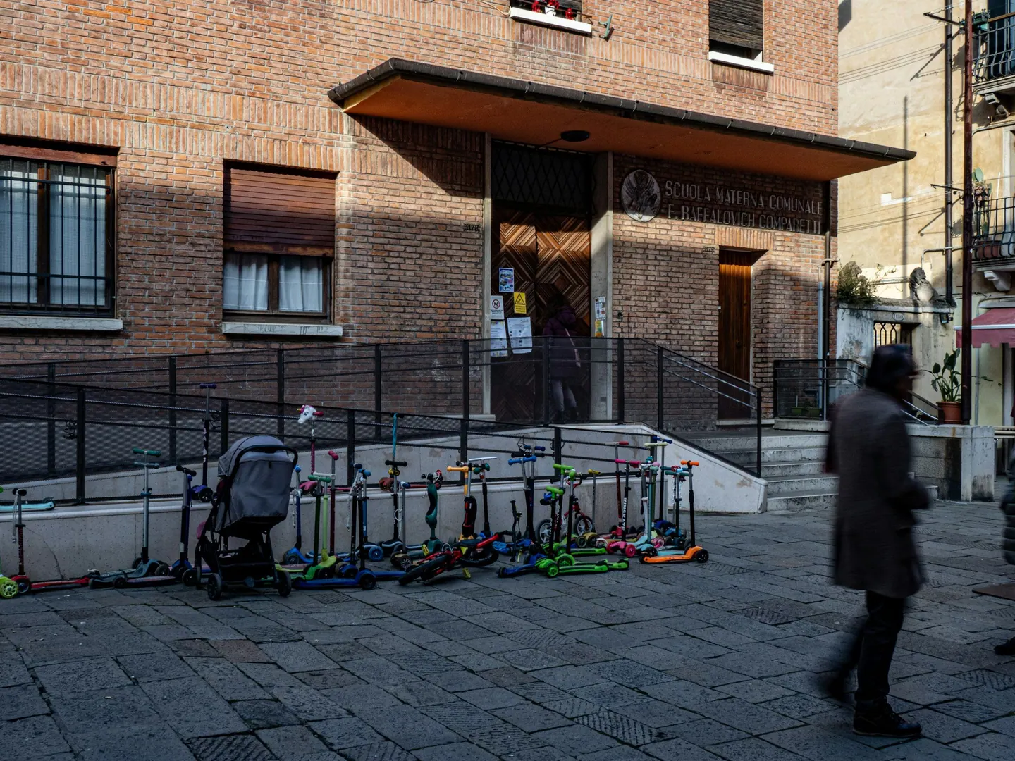 Entrada de un centro educativo de ladrillo con patinetes infantiles aparcados delante